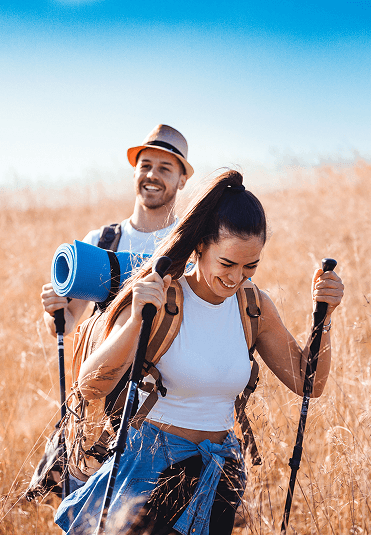 Man and woman walking through a field with hiking poles